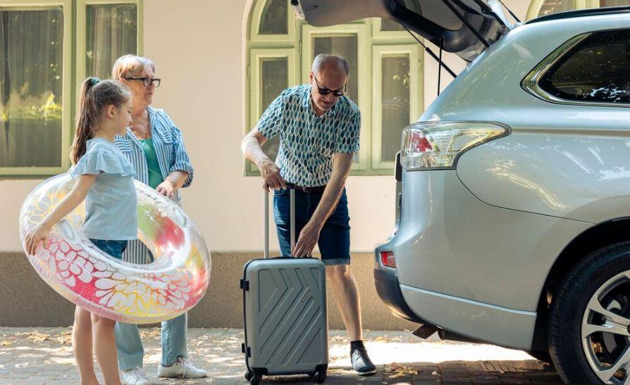 Babička, děda a vnučka balí věci do auta na dovolenou. Pojištění vozidel: Proč je důležité na dovolené pojištění technické asistence
