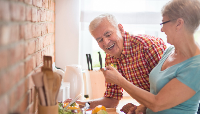 Starší muž ochutnává uvařené jídlo od své ženy.