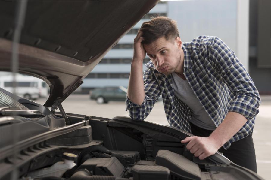 Mladý muž prohlíží bezradně motor u auta.